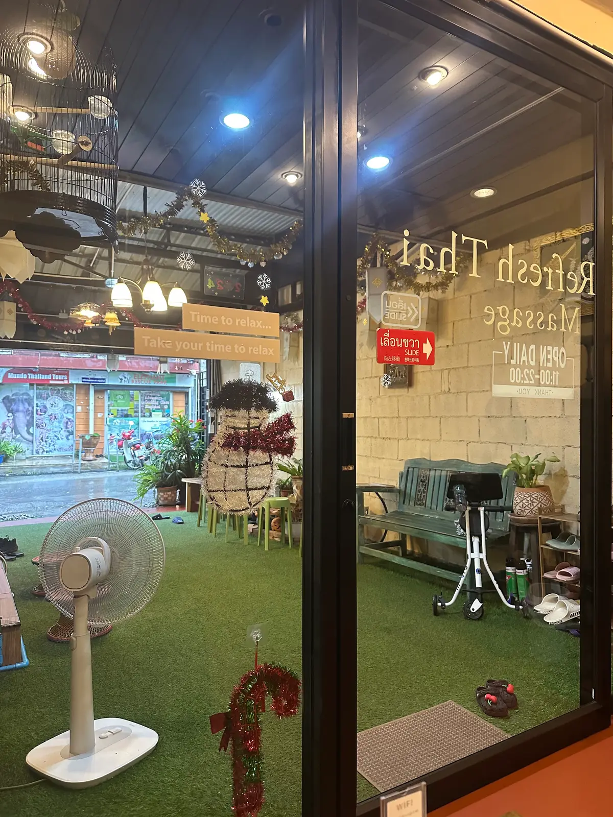 A glass shopfront with a sign reading Refresh Thai Massage and an artificial-grass seating area inside.