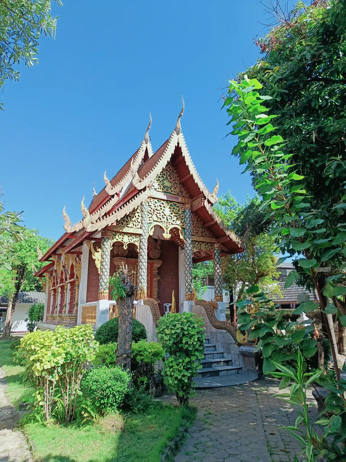 An ornate white and gold temple hall with a tiered roof among green plants.