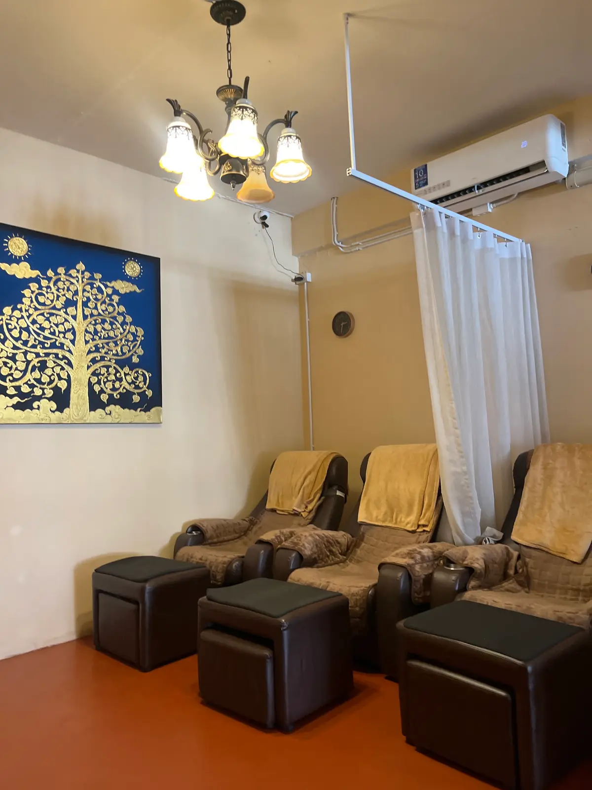 Three padded reclining chairs with footstools beside a curtain and a framed tree artwork.