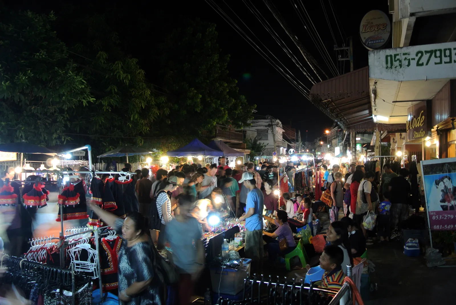 Crowd browsing lit stalls under tents along a narrow street at night.