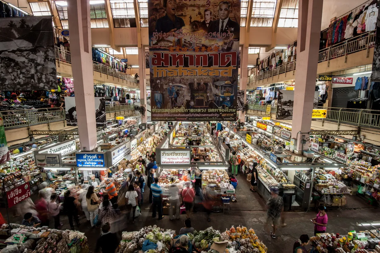 Shoppers walking through a covered hall of market stalls under a high ceiling.
