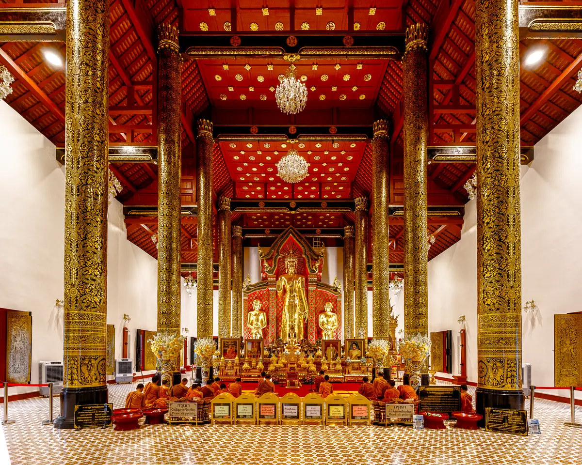 Hall interior with gilded columns, a red patterned ceiling and a golden Buddha on a stepped altar