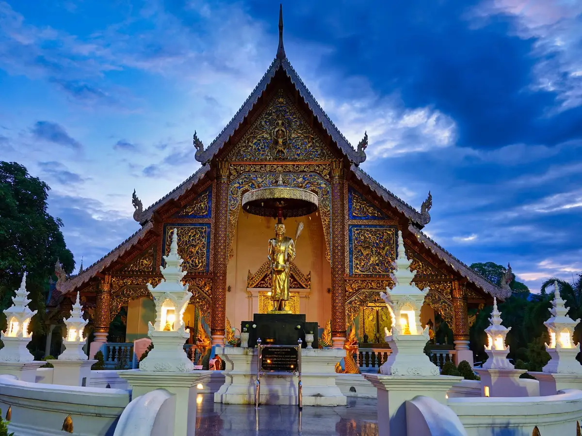 Ornate gabled temple front with gold decoration and a standing figure under a blue evening sky