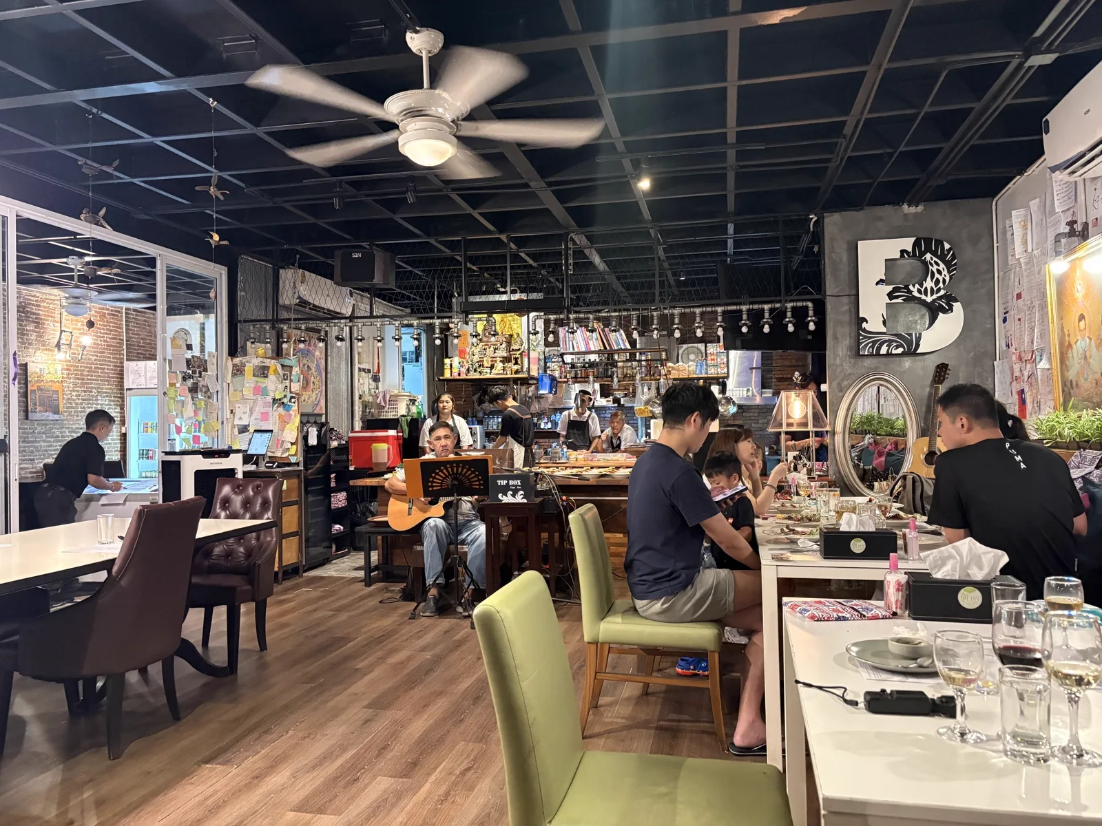 Restaurant interior with a dark ceiling, wooden floor, a guitarist and diners at tables