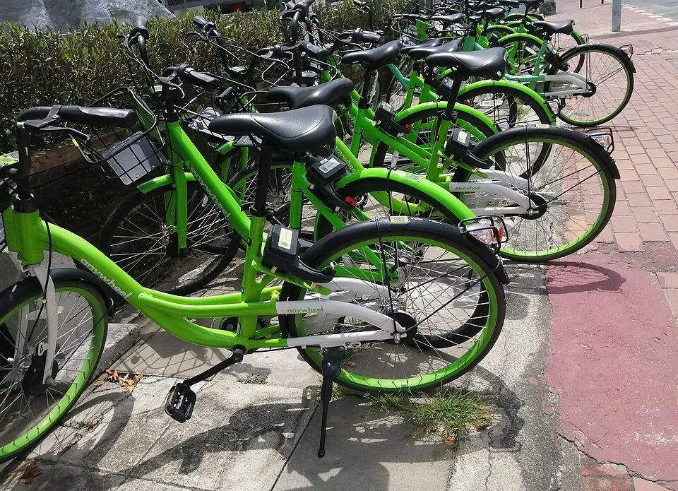 Row of green rental bicycles parked beside a red-tiled pavement